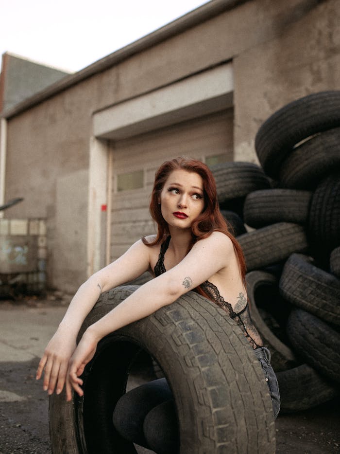 discover A fashionable woman poses with discarded tires in an industrial area, exuding confidence and style.