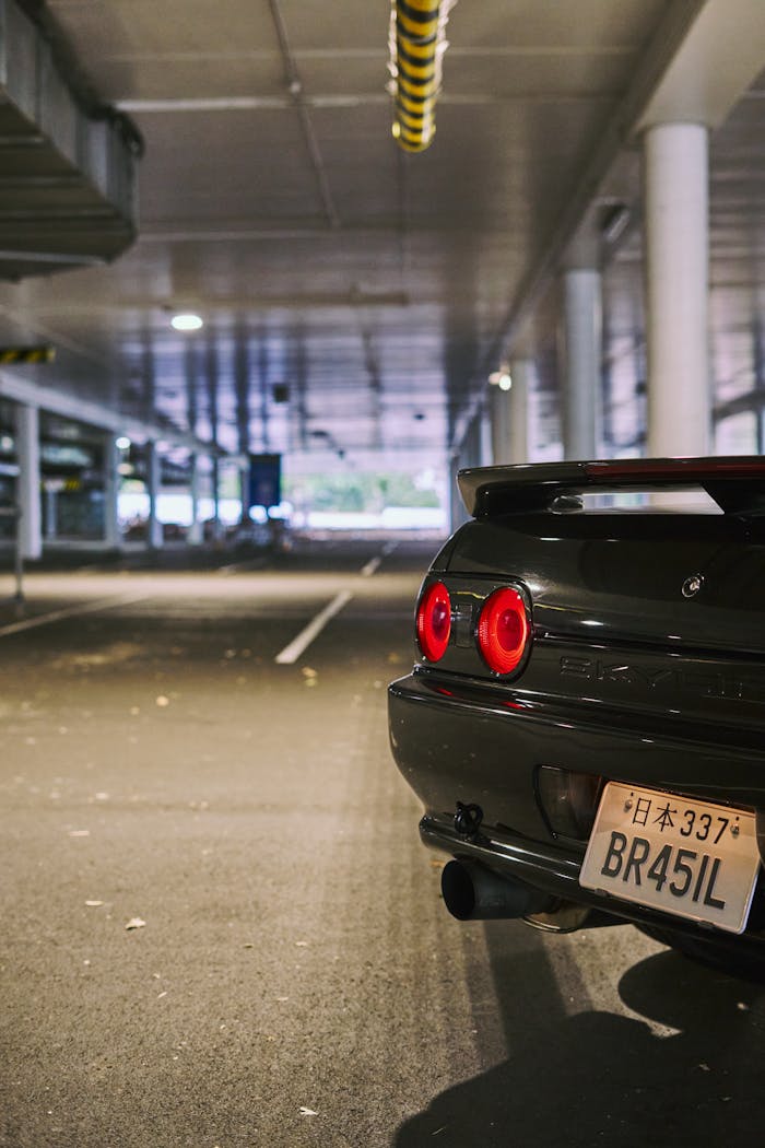 about-us Rear view of a black modified car with red taillights in an urban parking garage in Auckland.