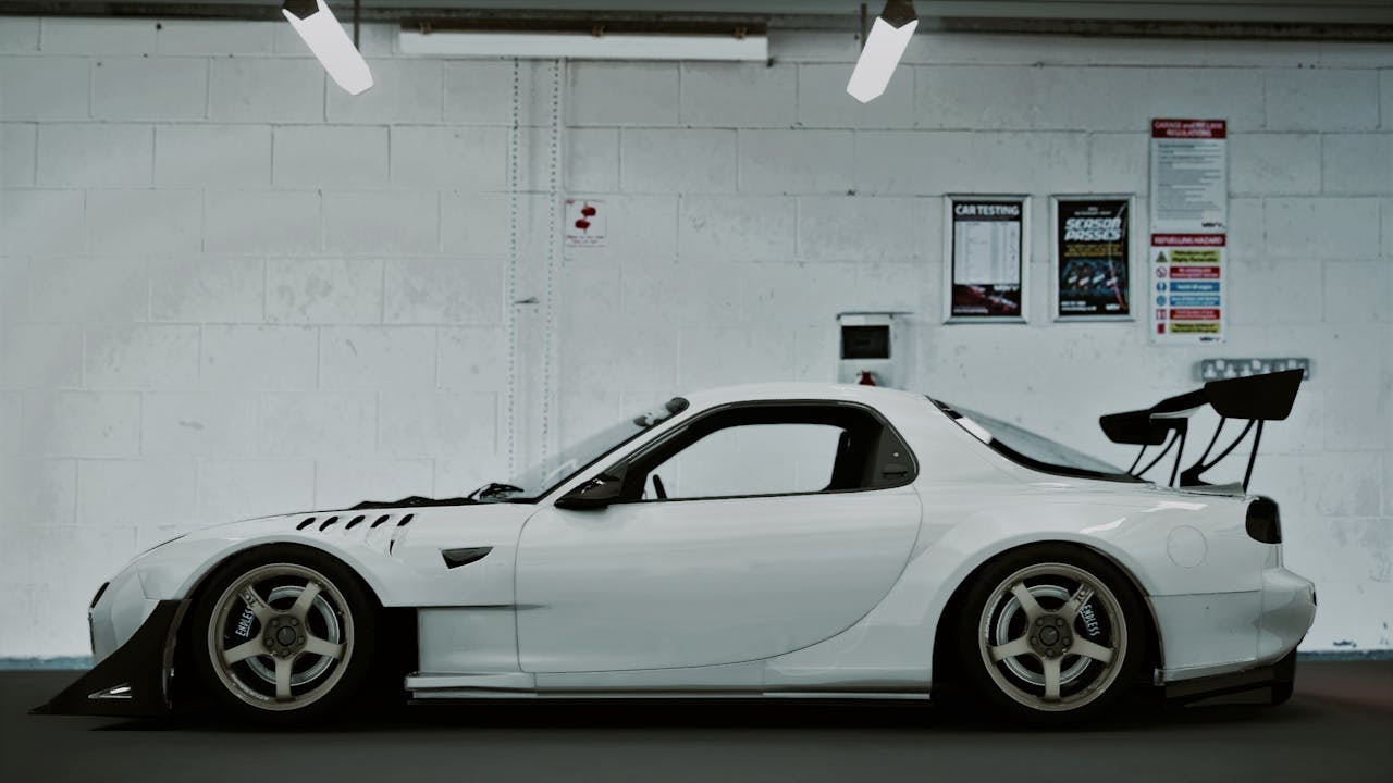 our-story Sleek white Mazda RX-7 parked indoors, captured in a side view.